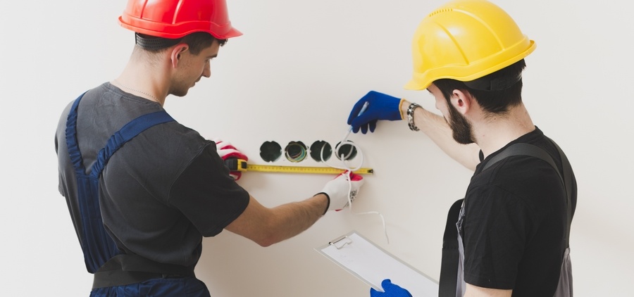 Deux électriciens mettent en place des prises électriques sur un chantier